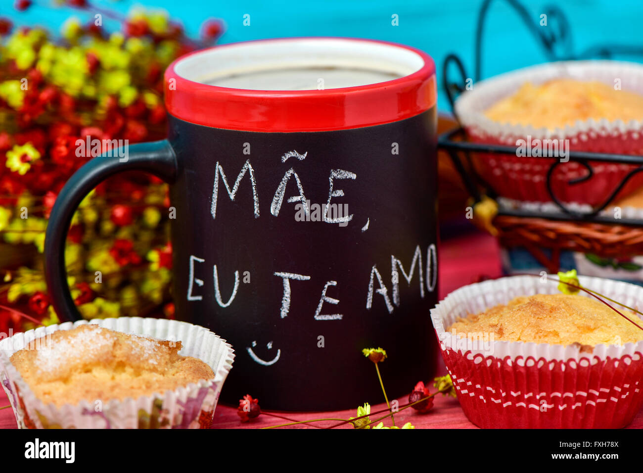 the sentence mae eu te amo, I love you mom in portuguese handwritten with chalk in a black mug with coffee, with some muffins in Stock Photo