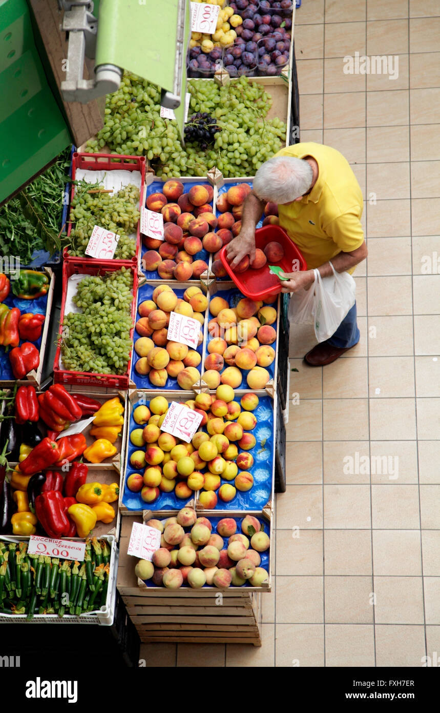 elderly customer browses fruit and vegetable goods displayed on stall inside an indoor market in Rome, Italy Stock Photo
