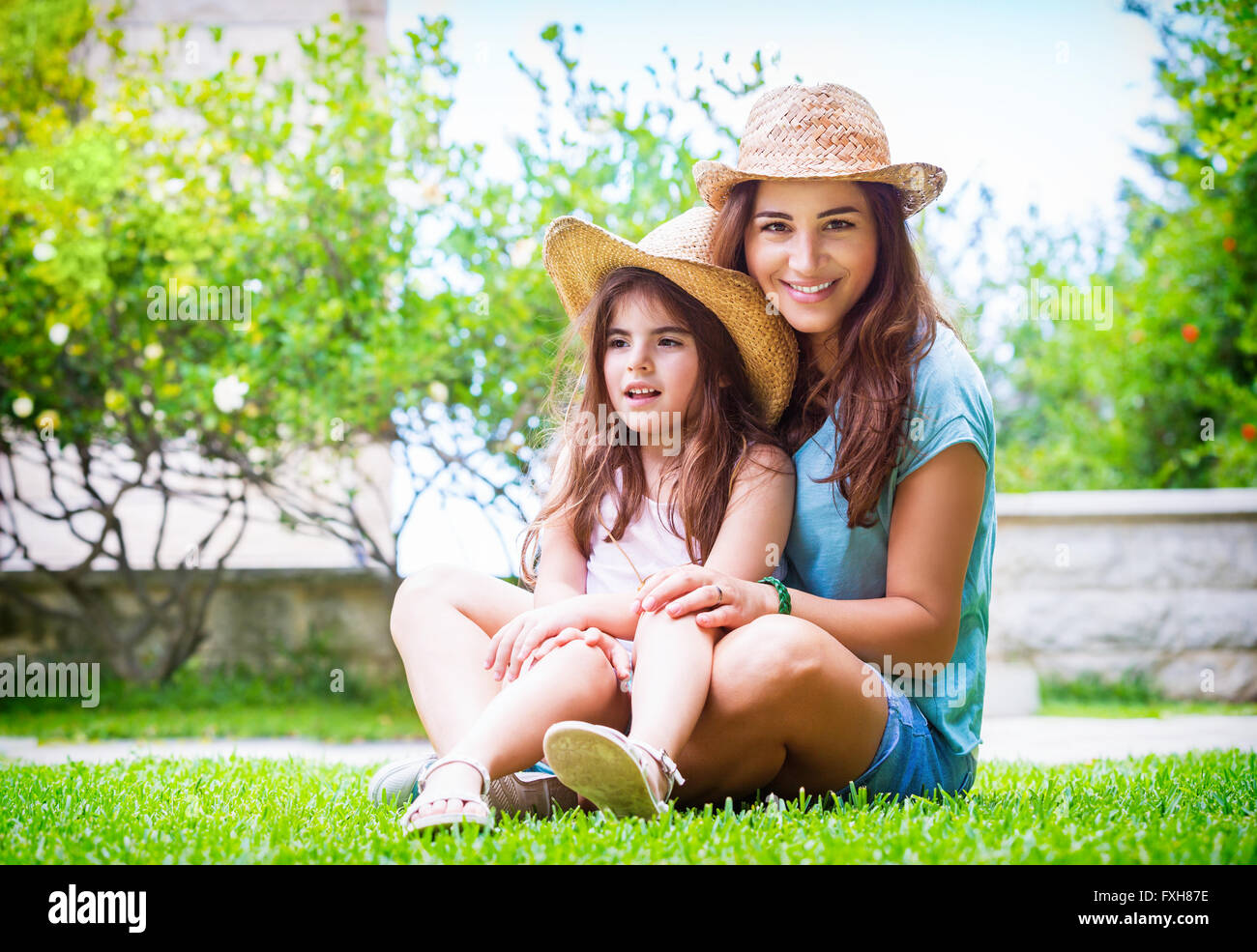 Happy family in the garden, beautiful mother with her little cute daughter sitting on fresh green grass on backyard Stock Photo
