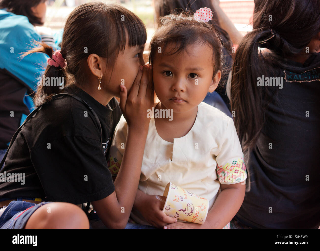 One young girl whispers to another at a funeral ceremony in Tana Toraja. Stock Photo