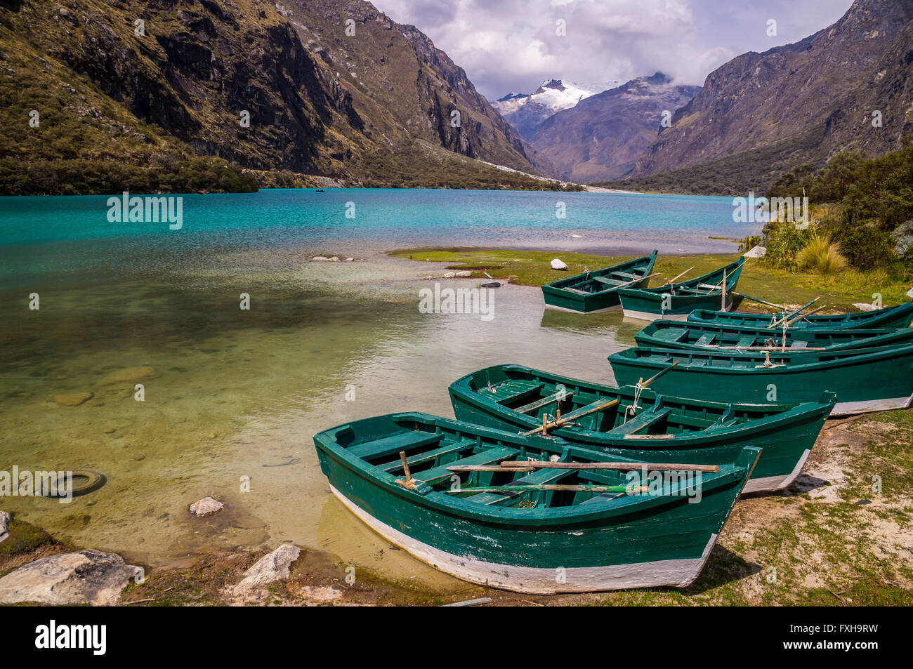 Huaraz, PERU in November 2015: Six green boats are waiting to be sailed across the blue glacier lagoon in the Peruvian Andes. Hu Stock Photo