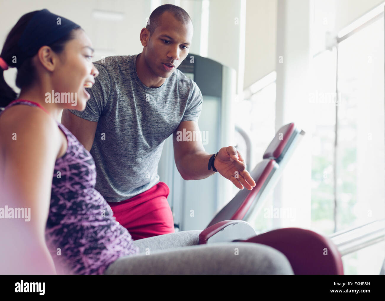 Personal trainer guiding woman on exercise equipment at gym Stock Photo