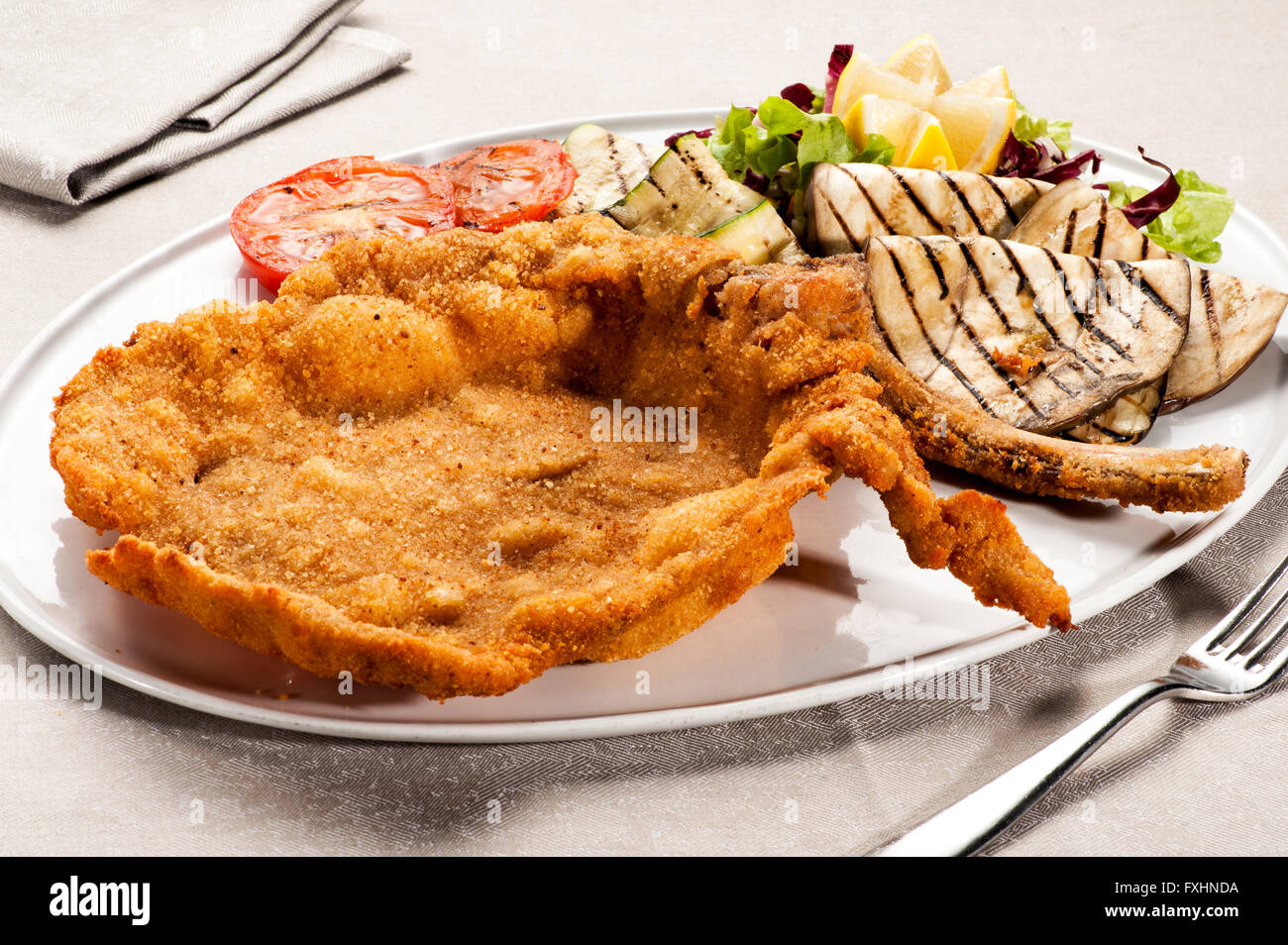 Single serving of fried Milanese cotoletta with tomatoes, lettuce and other ingredients on plate with silverware Stock Photo