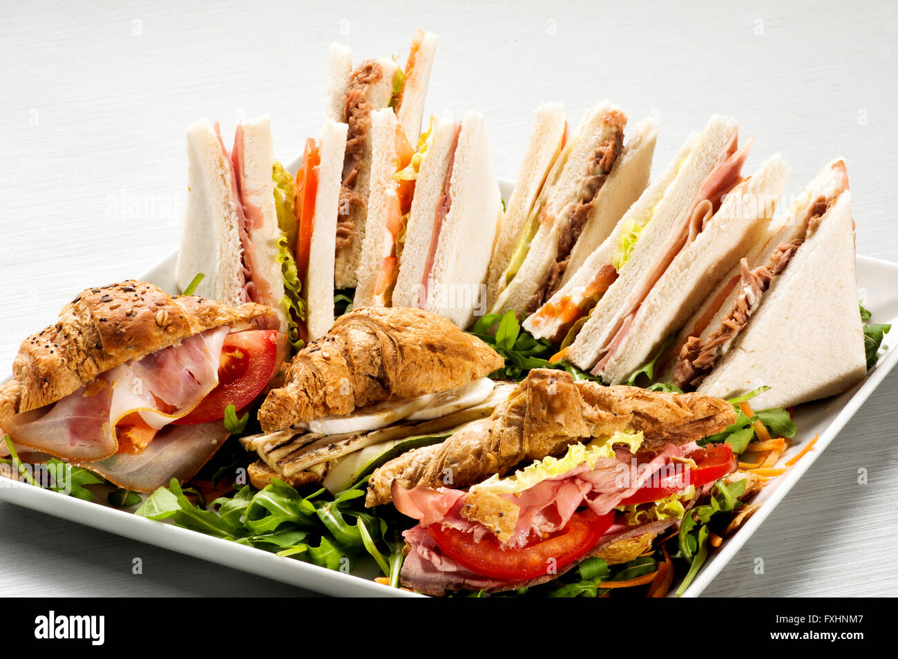 Large tray full of delicious white bread and croissant sandwiches stuffed with meat, tomatoes and vegetables Stock Photo