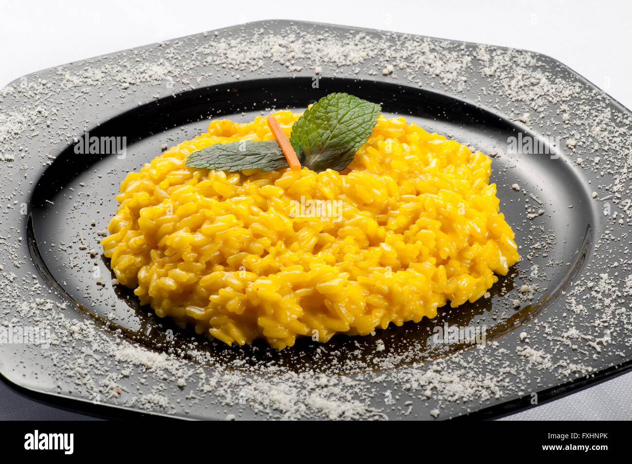 Hexagonal black cast iron plate with yellow risotto rice and carrot mint garnish on top Stock Photo