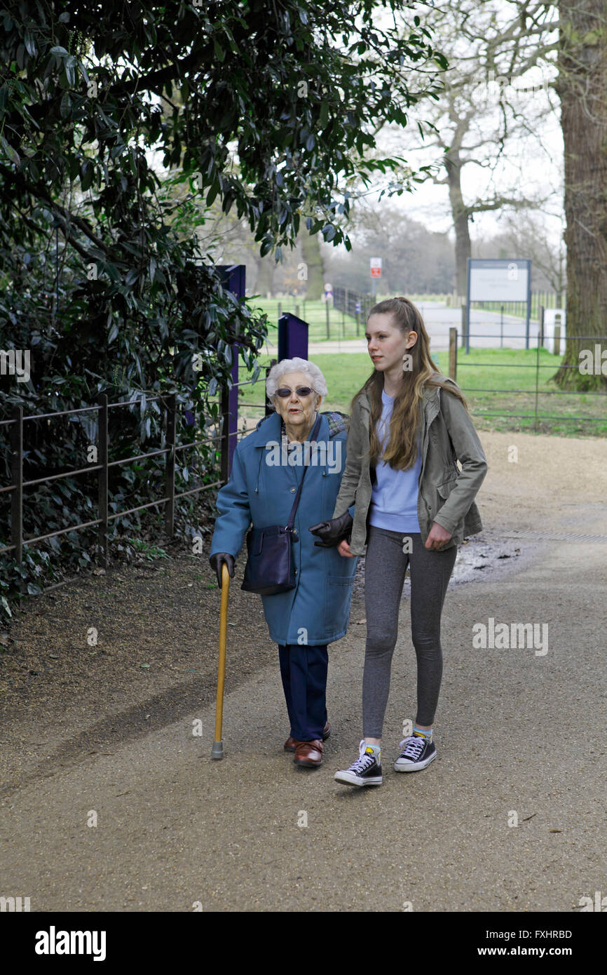 A grandmother and granddaughter walking in a park. Octogenarian with a teenage carer hepler. Stock Photo