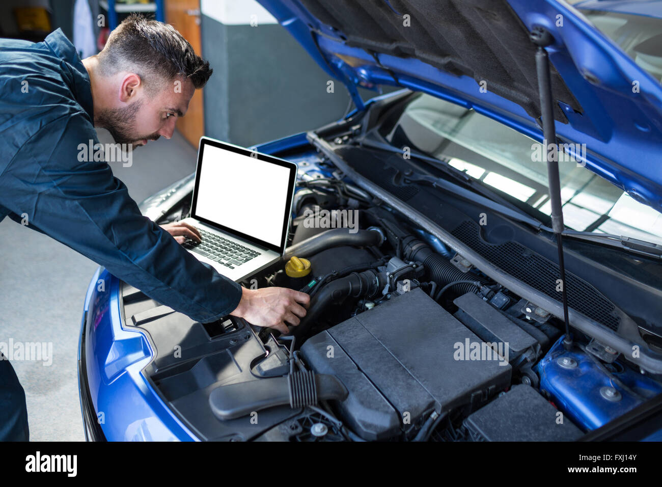 Mechanic examining car engine with help of laptop Stock Photo