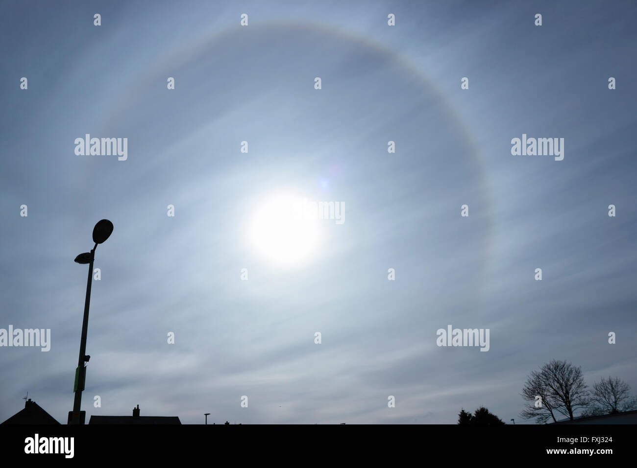 An unusual 22° halo circular rainbow around the sun caused by diffraction of light through ice crystals in the atmosphere. Sun Dog. Stock Photo