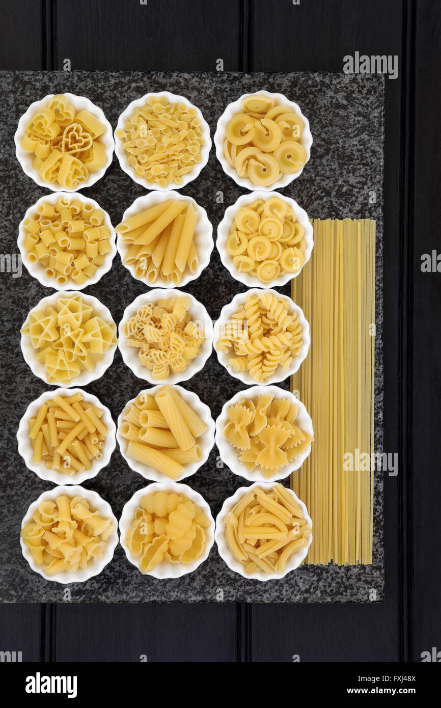Pasta spaghetti dried food selection in porcelain crinkle bowls on a marble slab over dark wood  background. Stock Photo