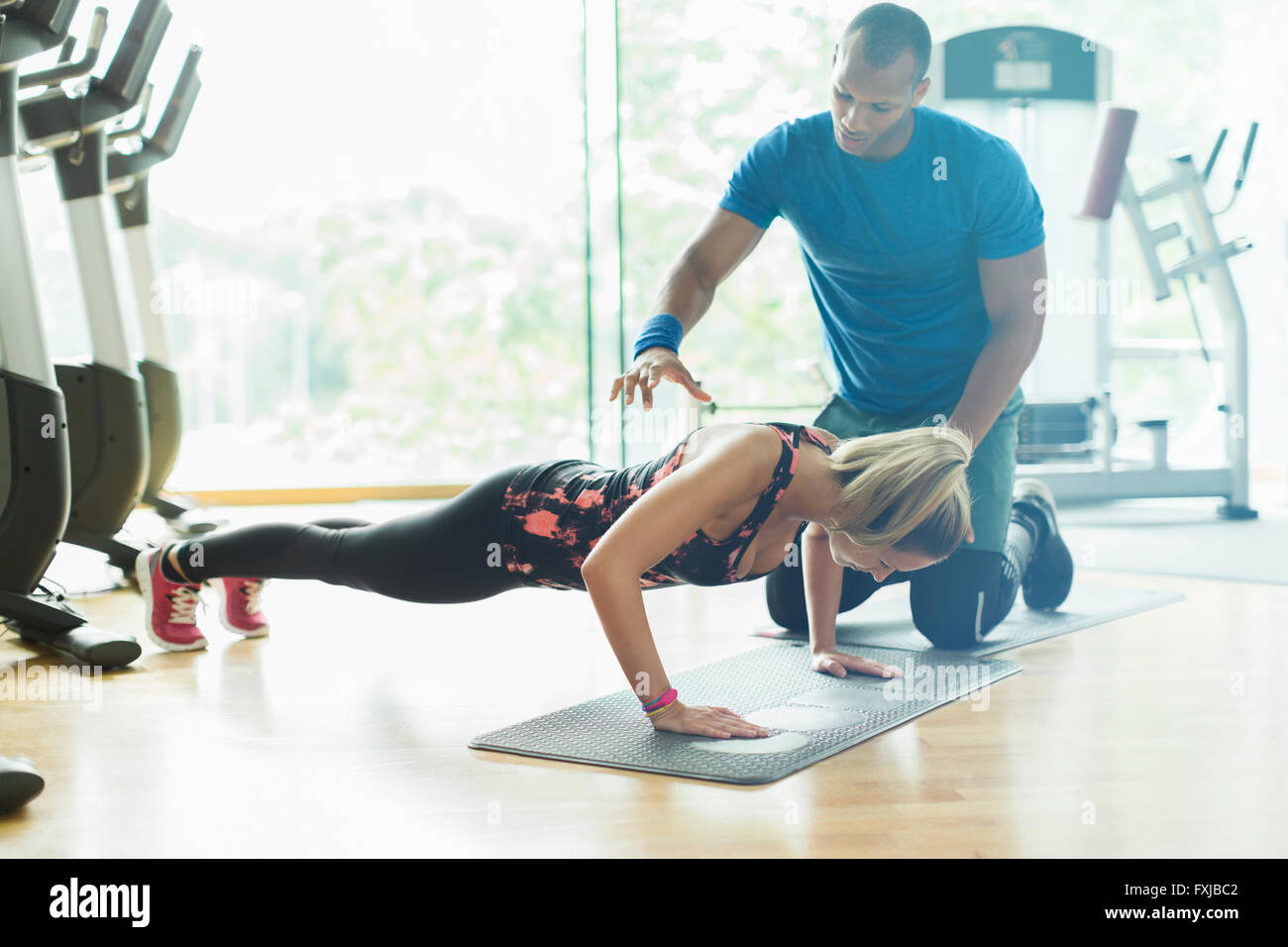 Personal trainer guiding woman doing push-ups at gym Stock Photo