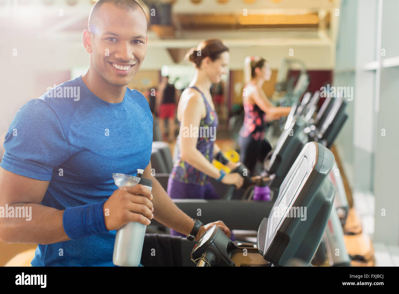 Portrait smiling man with water bottle on treadmill at gym Stock Photo