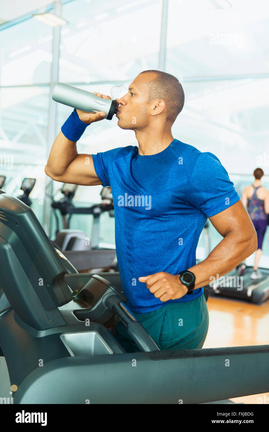 Man drinking water on treadmill at gym Stock Photo