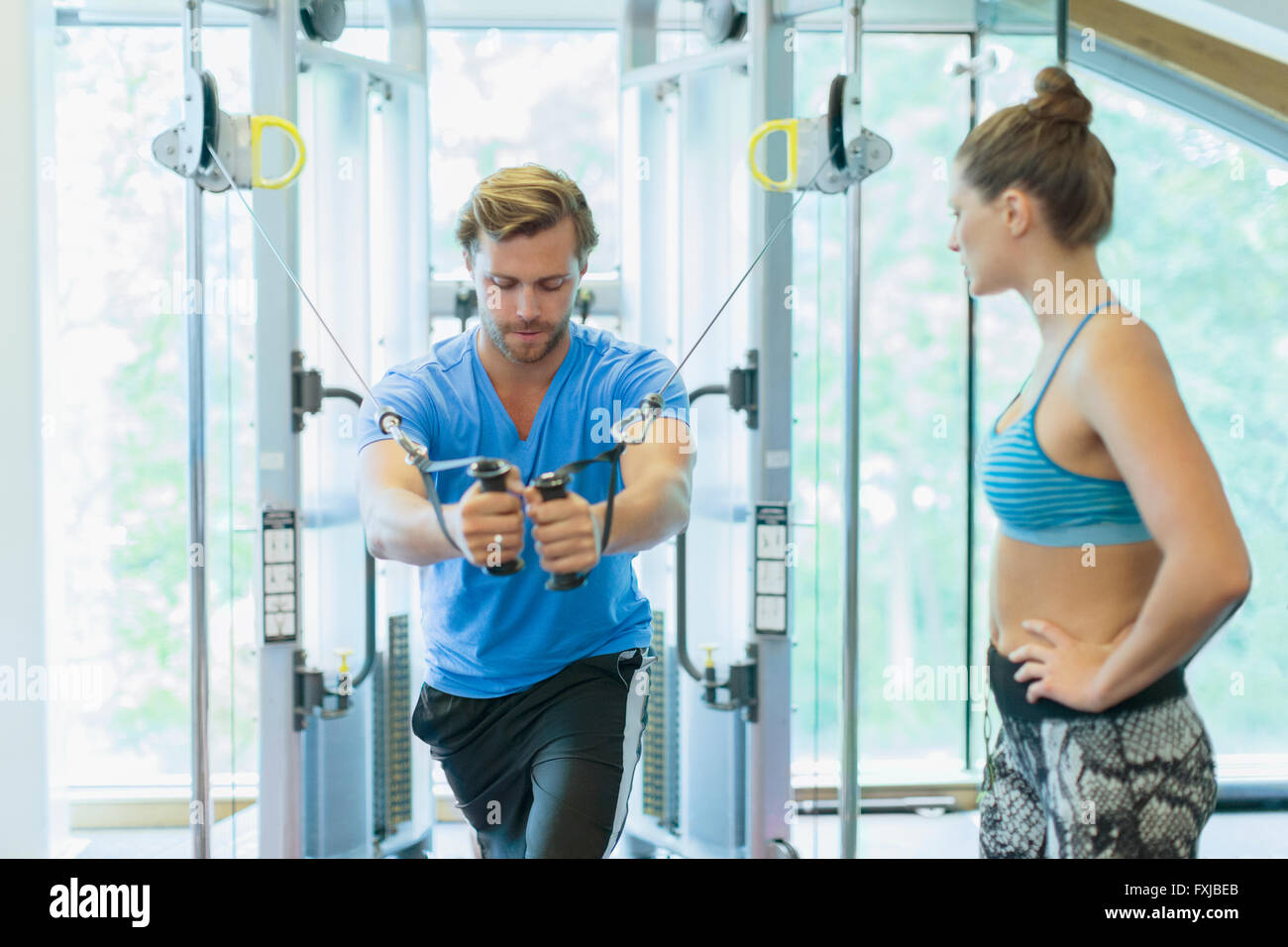 Personal trainer guiding man using cable exercise machine at gym Stock Photo
