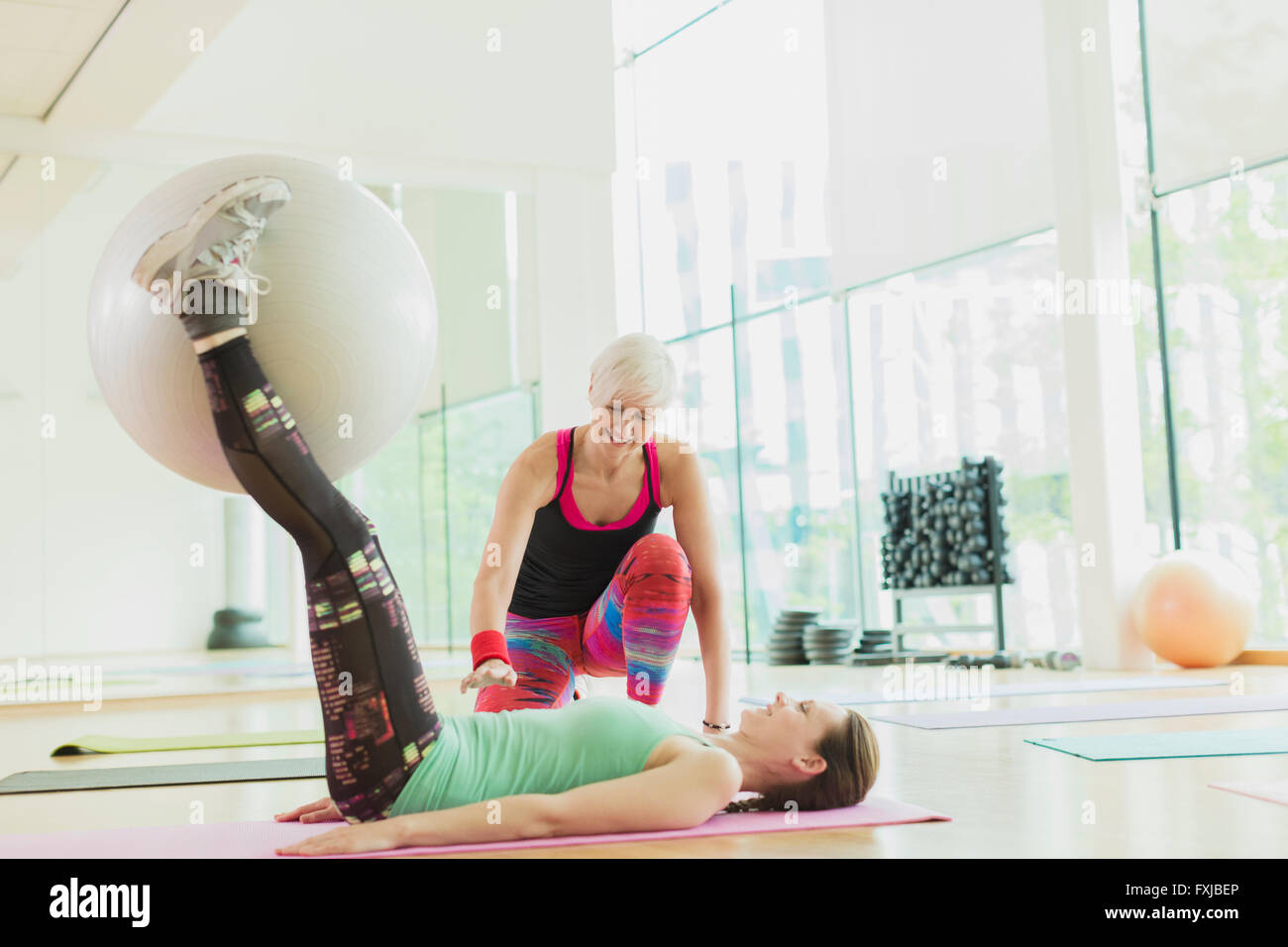 Personal trainer guiding woman with fitness ball between legs Stock Photo