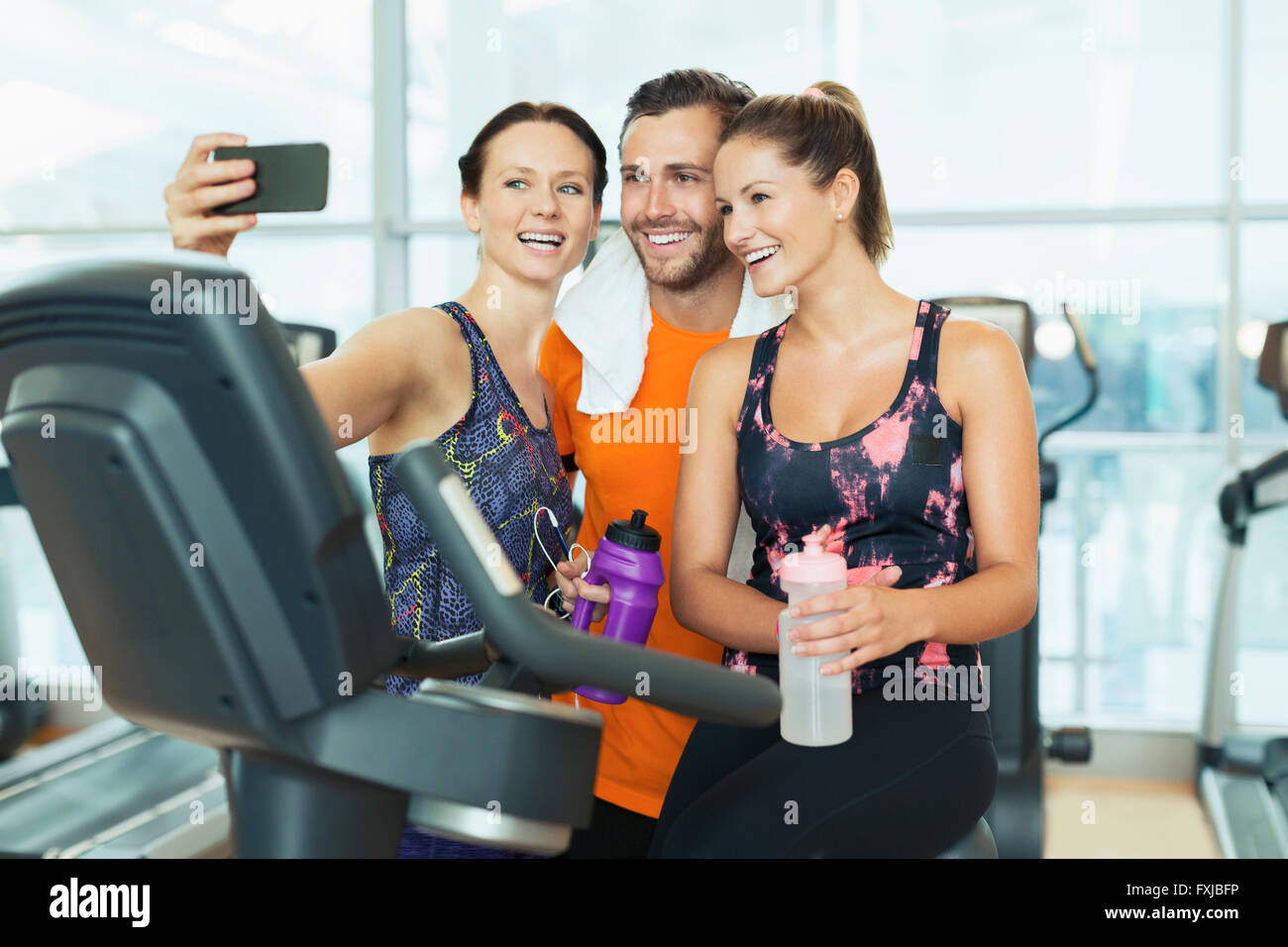 Smiling friends taking selfie at exercise bike in gym Stock Photo