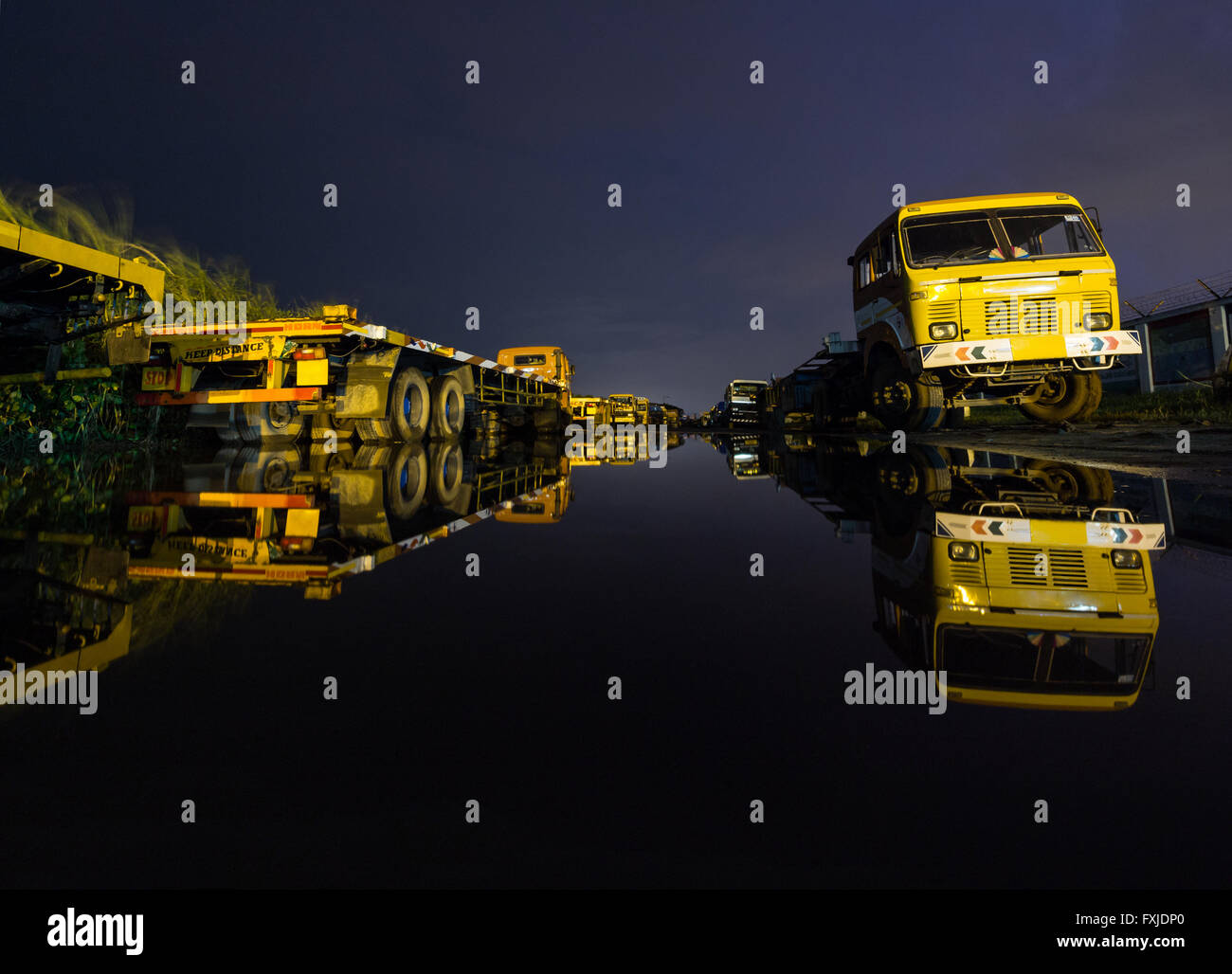 Trucks parked on each side of the road seen reflected on a large puddle. Stock Photo