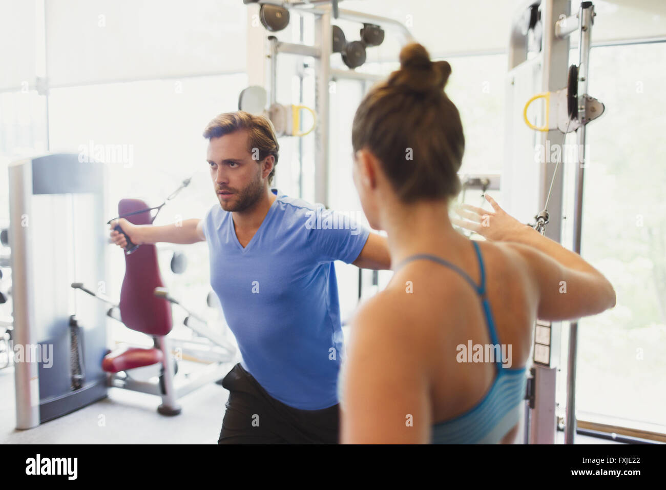 Female personal trainer guiding man doing cable chest fly at gym Stock Photo