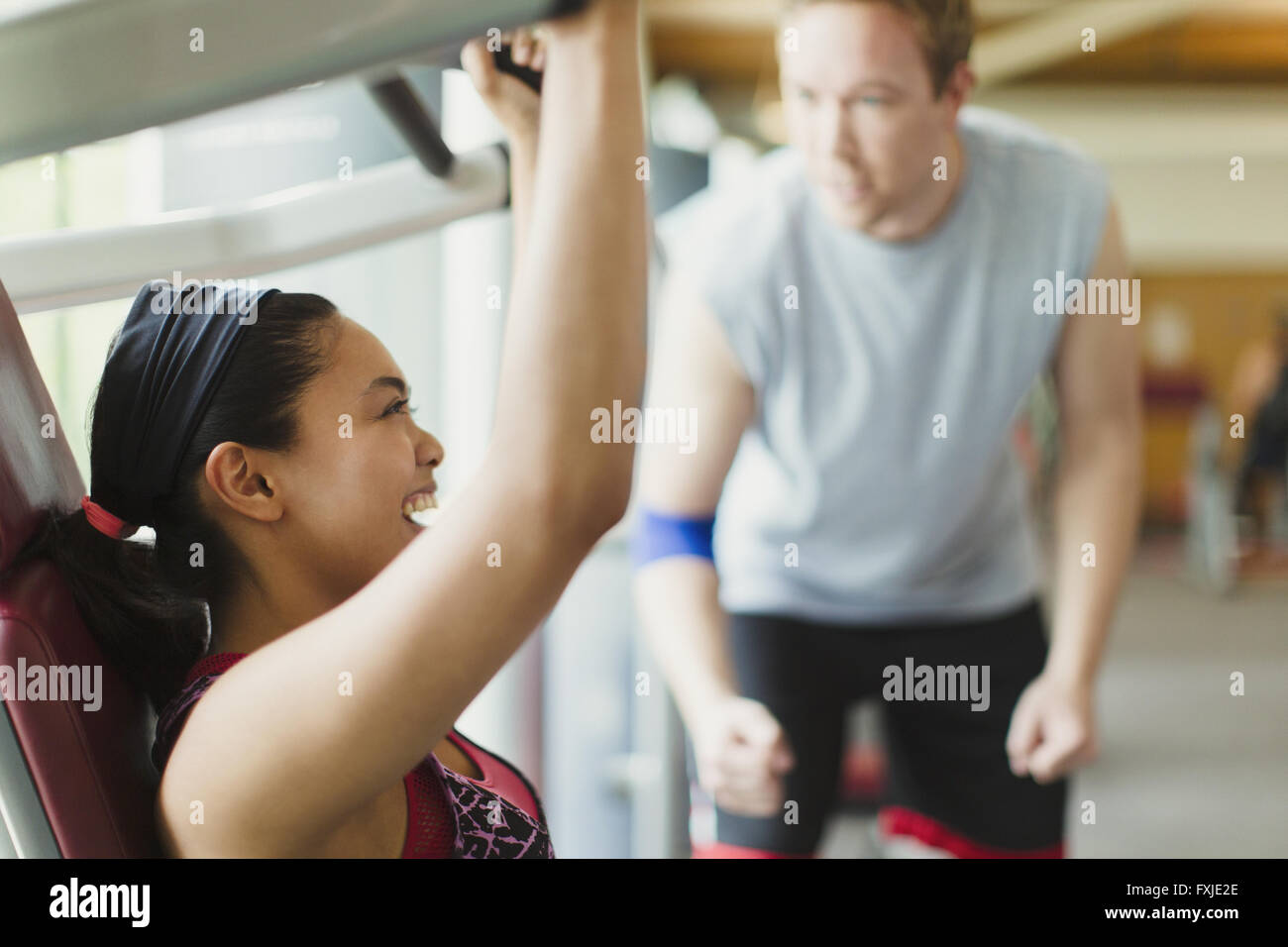 Personal trainer guiding enthusiastic woman using exercise equipment at gym Stock Photo