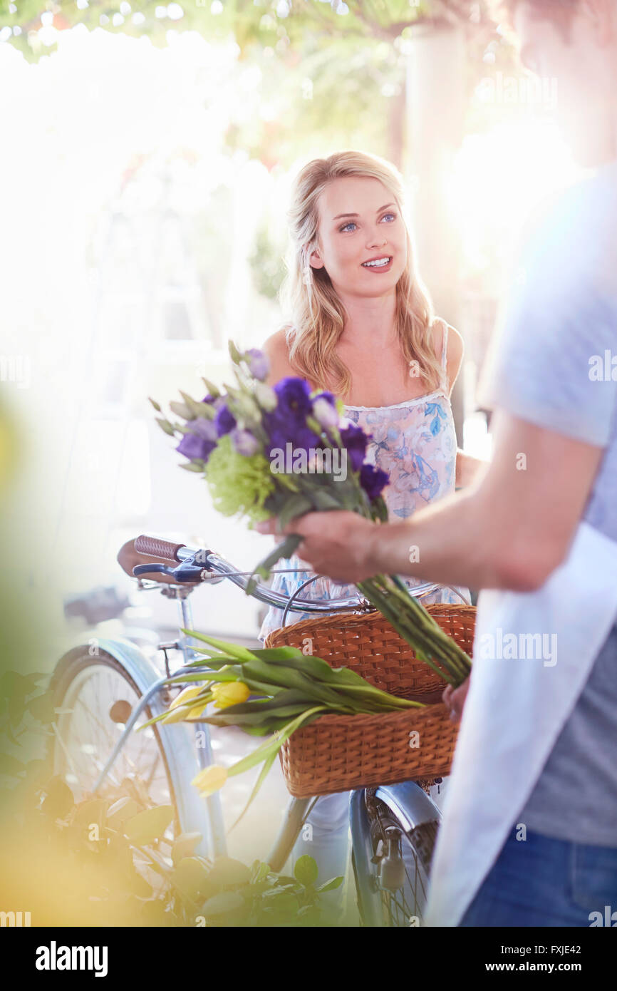 Florist placing flowers in basket on woman’s bicycle Stock Photo