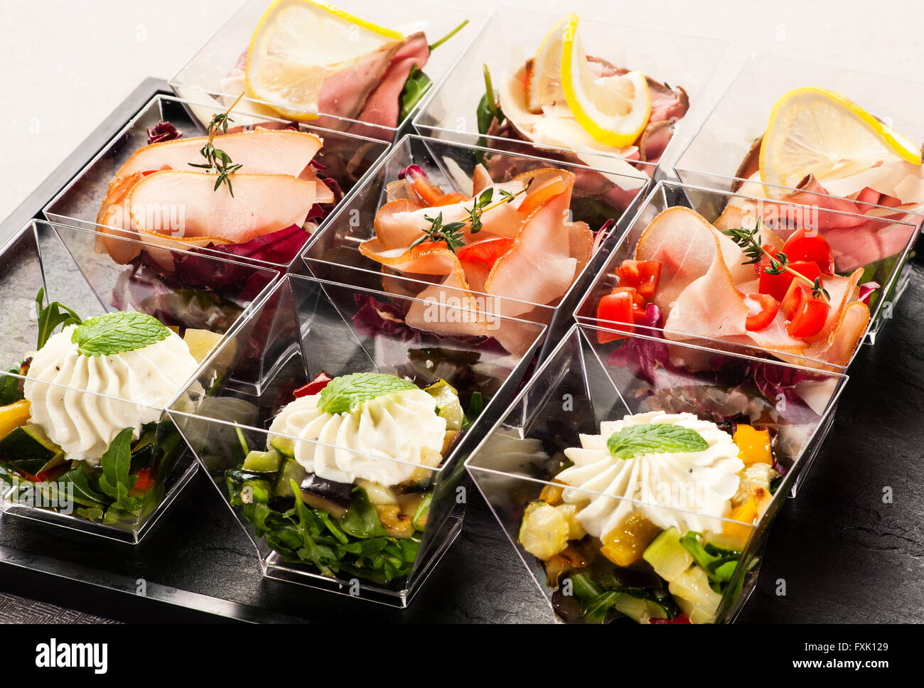 Cute rectangular slanted glass containers filled with delicious appetizers made of fruit, meat and herbs Stock Photo
