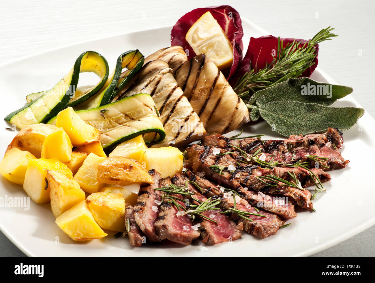 Single serving of rare cooked steak slices, baked yellow potato, eggplant and squash with herbs