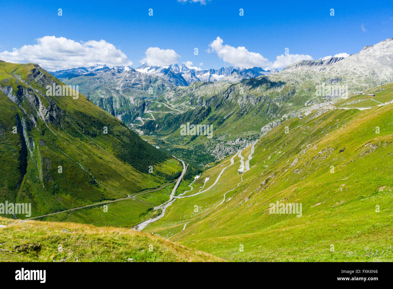 Road leading to Furka Pass winding up a green mountain slope, high mountains in the distance, Andermatt, Uri, Switzerland Stock Photo