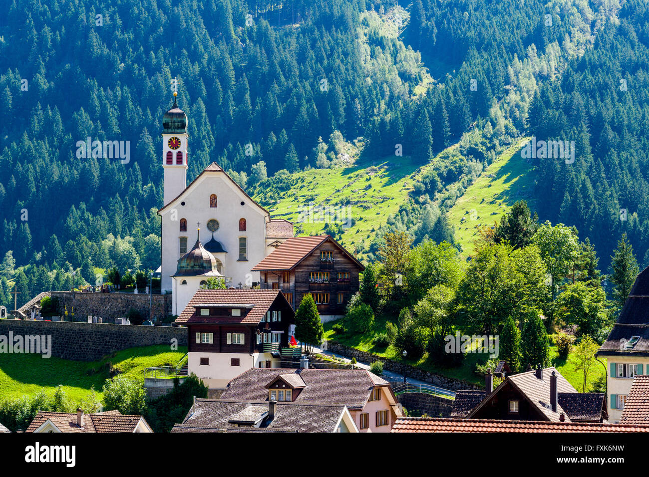 Village with church, high altitude landscape with mountains, green meadows and trees, Wassen, Graubünden, Switzerland Stock Photo