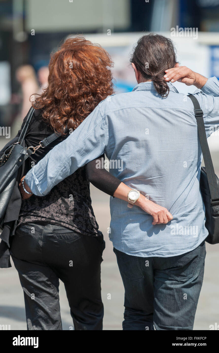 Back view of couple walking with arms around each other. Stock Photo