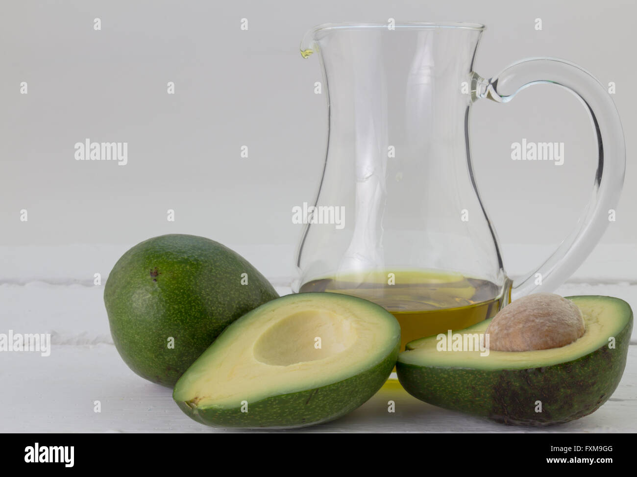 Imperfect avocados and a jug of avocado oil isolated on rustic white background Stock Photo