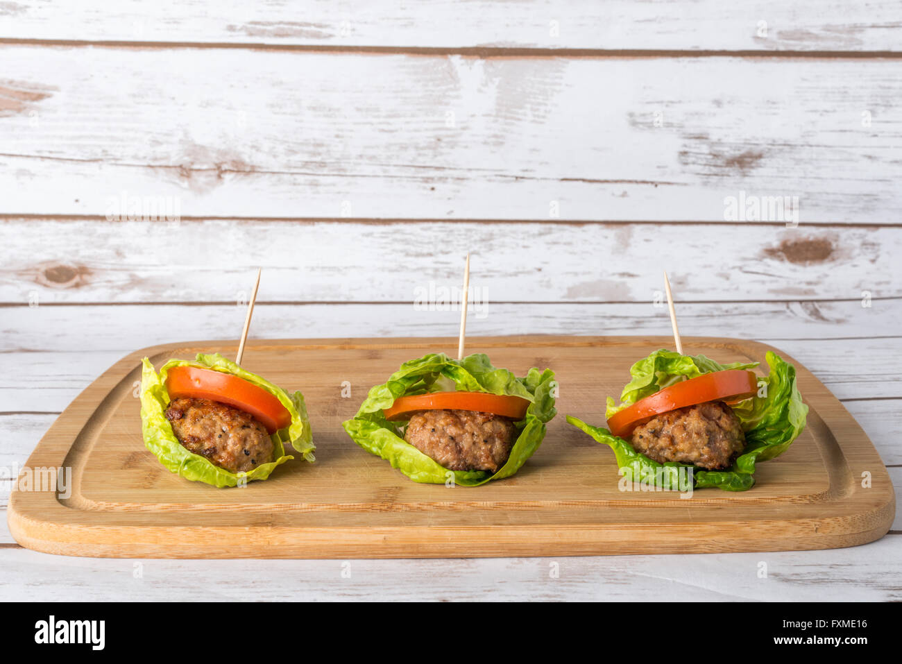 Bunless burger with bun replaced with lettuce leaves on wooden board Stock Photo