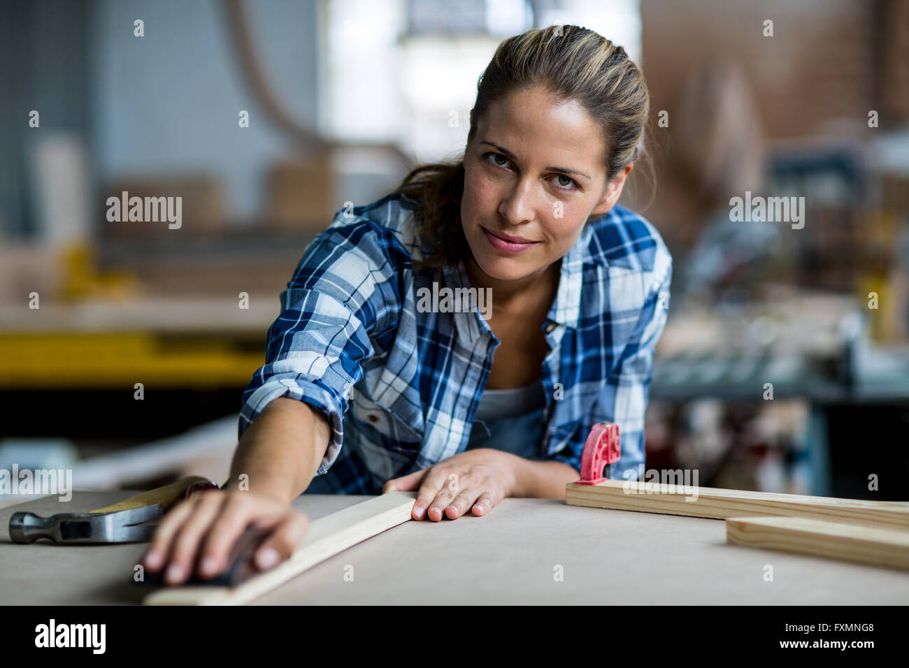 Female carpenter rubbing wooden plank with sanding block Stock Photo