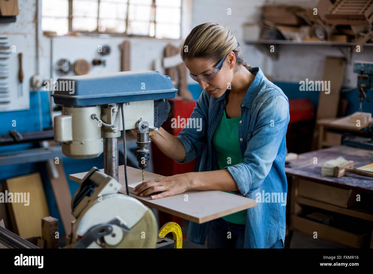 Female carpenter drilling a hole in a wooden plank Stock Photo