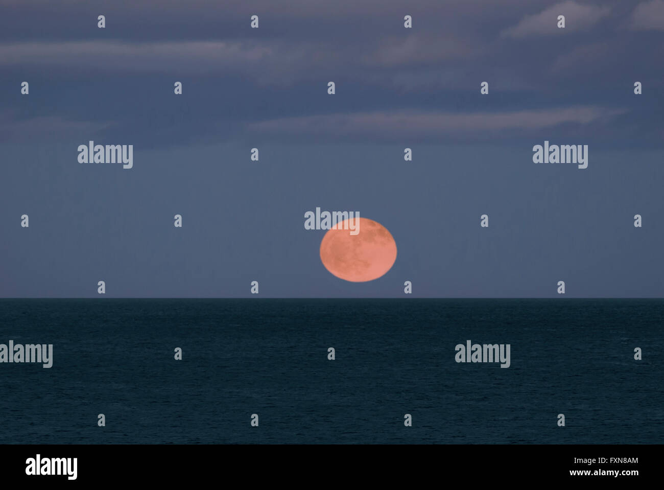 The full moon rising over the sea, its image refracted by the atmosphere Stock Photo