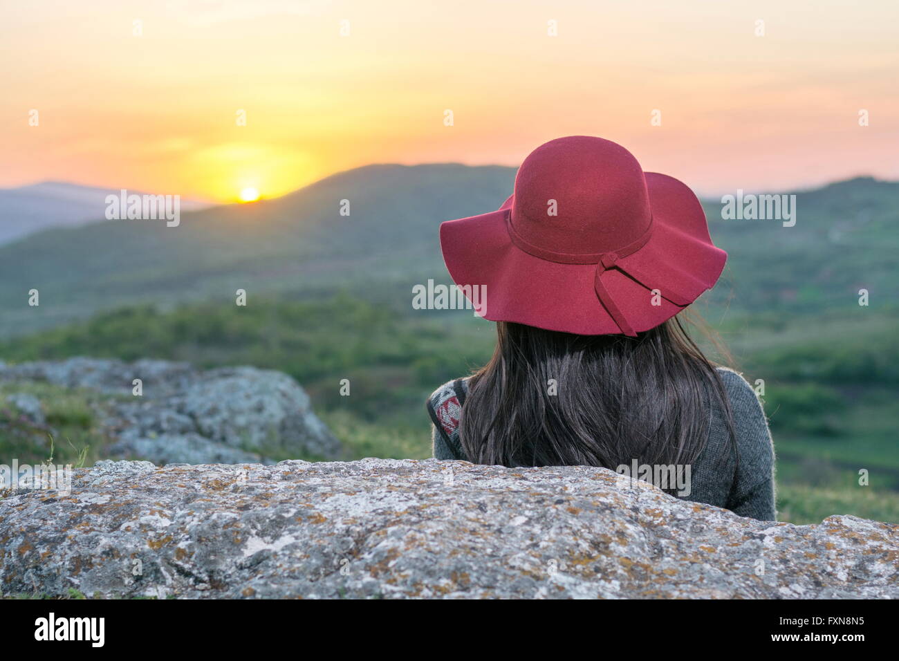 Female hiker enjoying sunset while sitting on a rock Stock Photo