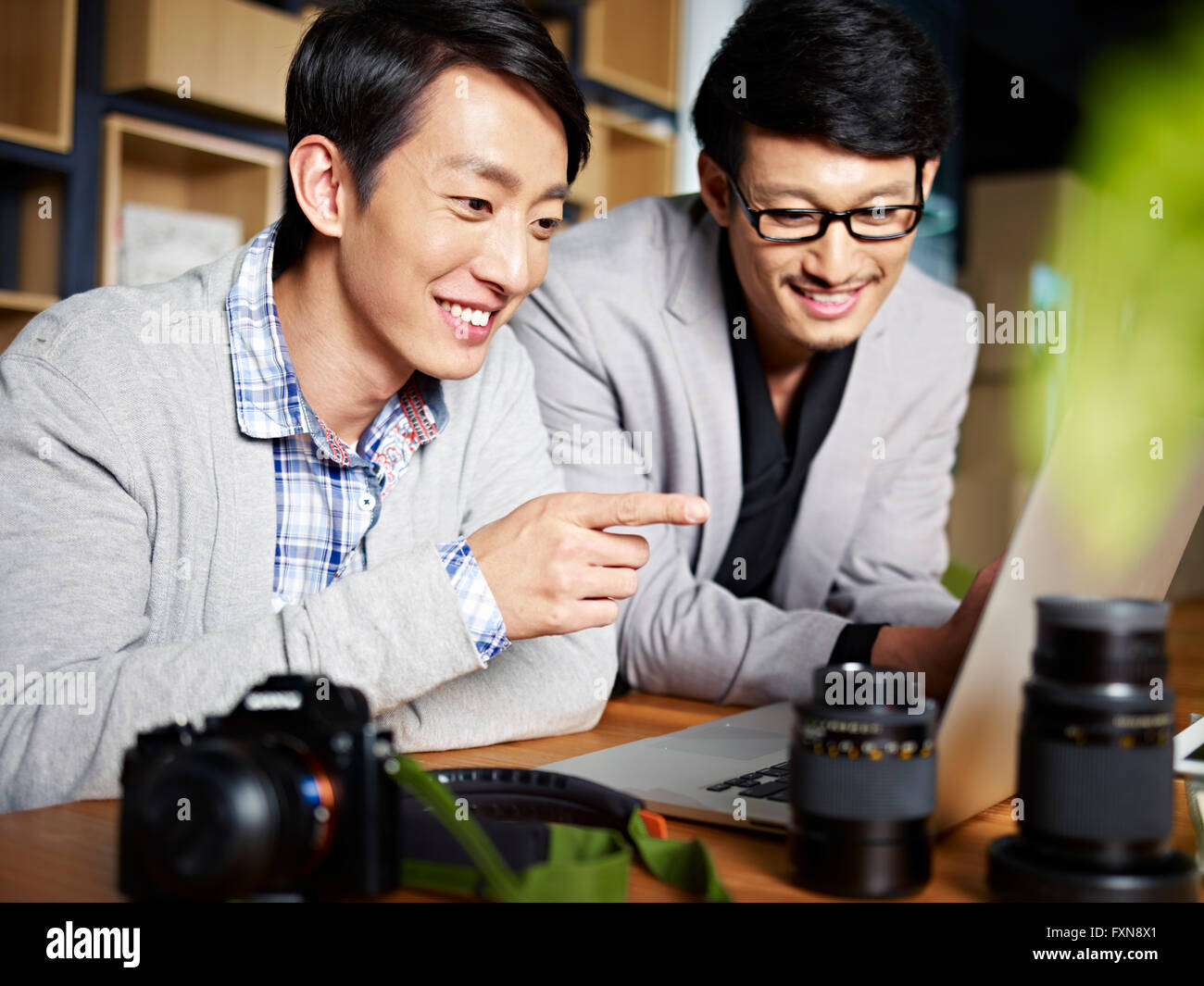 two young asian photographers designers selecting pictures using laptop computer in studio. Stock Photo