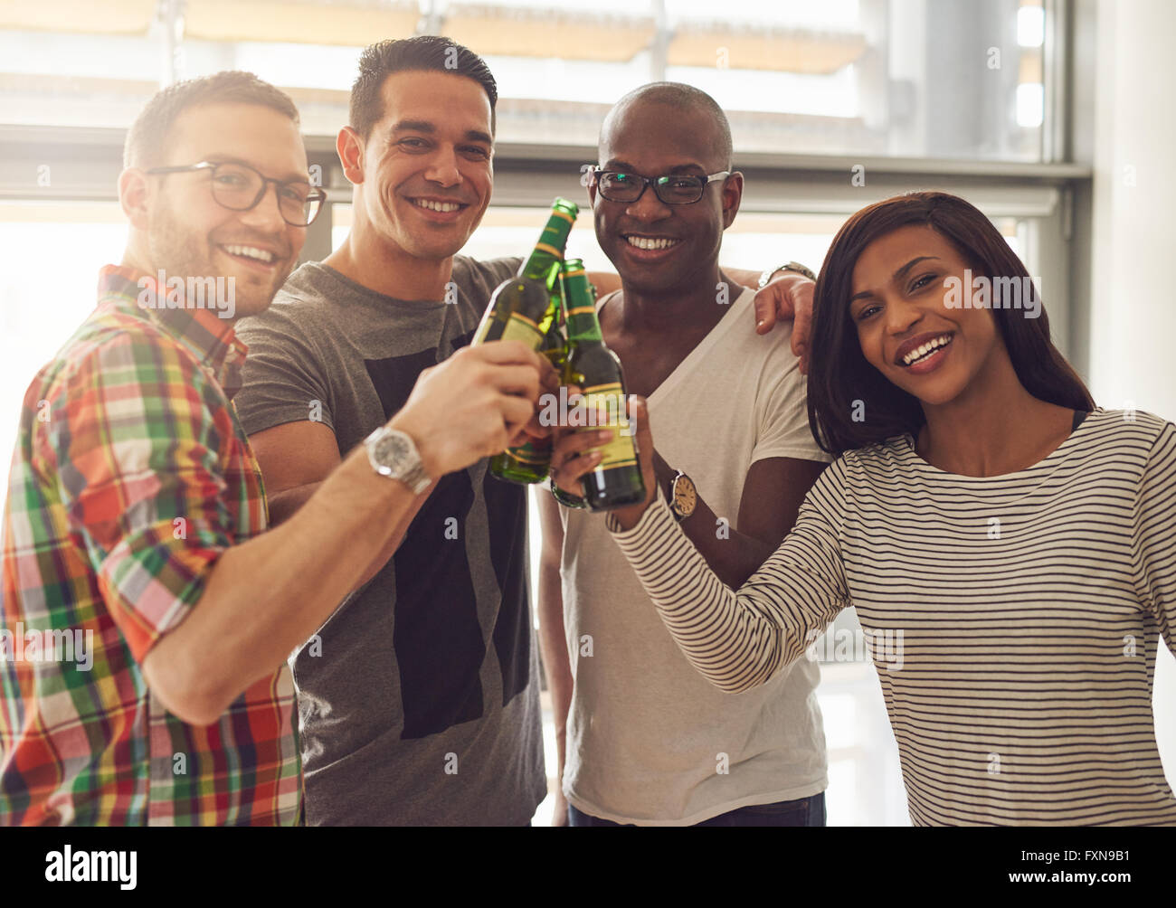 Diverse group of four young smiling friends in casual outfits tapping green glass beer bottles Stock Photo