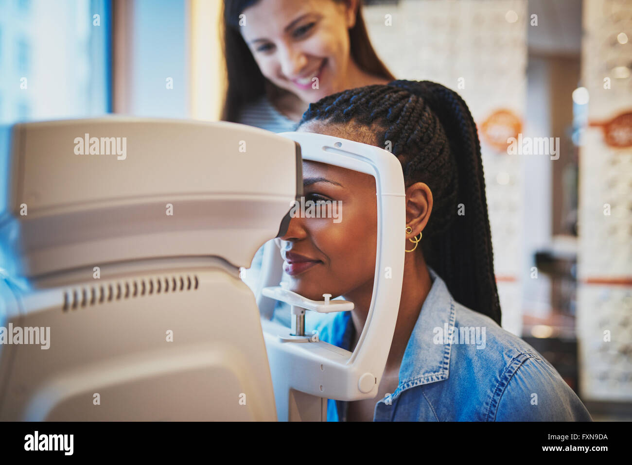 Pretty young black woman presses her forehead to optical machine to take eye exam Stock Photo