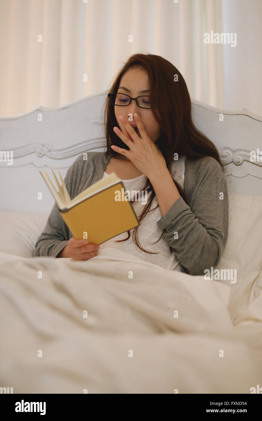 Young attractive Japanese woman reading in bed Stock Photo