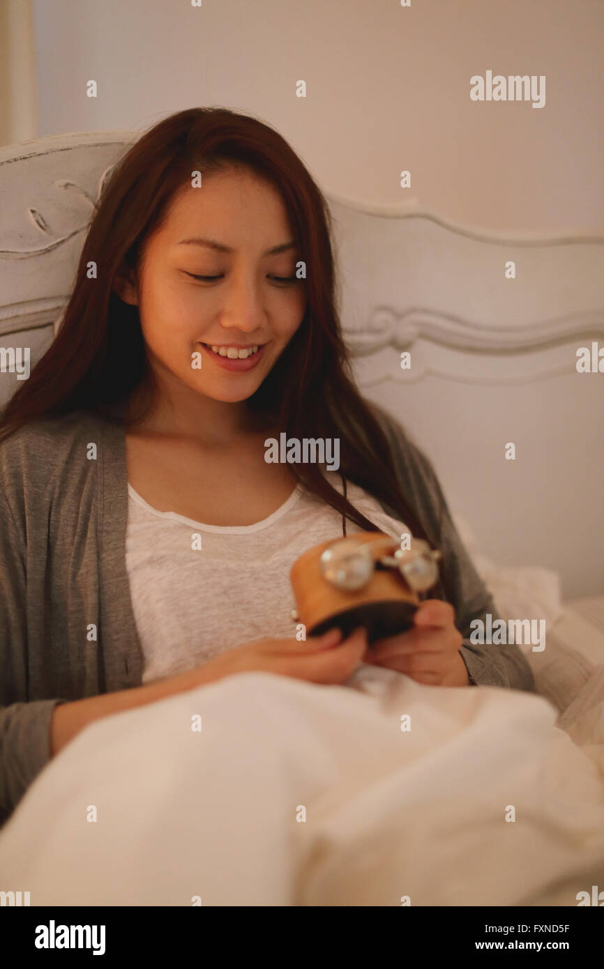 Young attractive Japanese woman setting alarm clock in bed Stock Photo