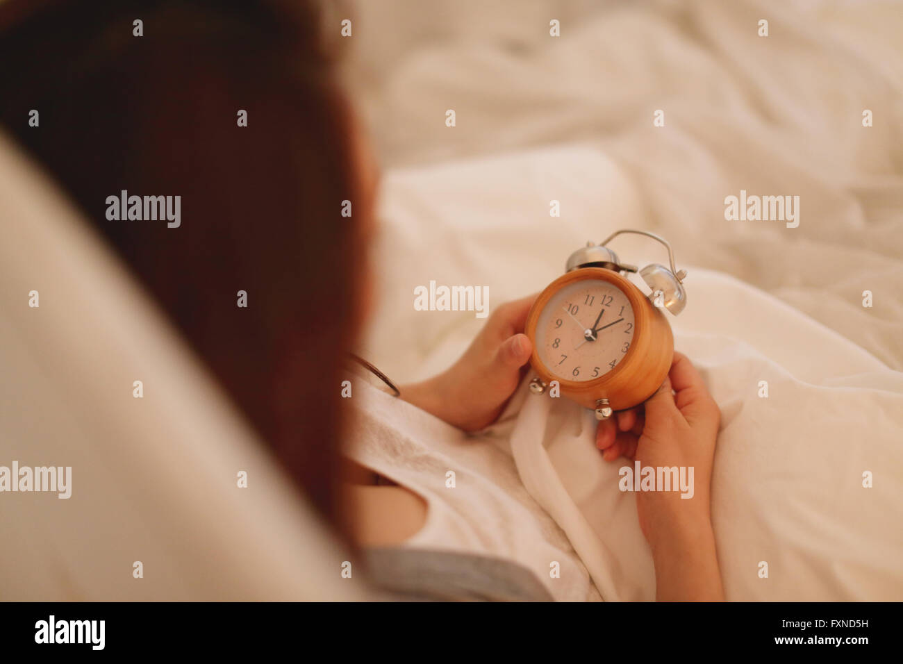 Young attractive Japanese woman setting alarm clock in bed Stock Photo