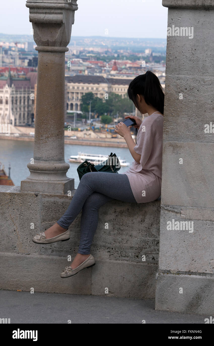 A young Asian tourist admires the city view from the Fishermen's Bastion at Buda Castle hill in Budapest, Hungary.  Buda Castle Stock Photo