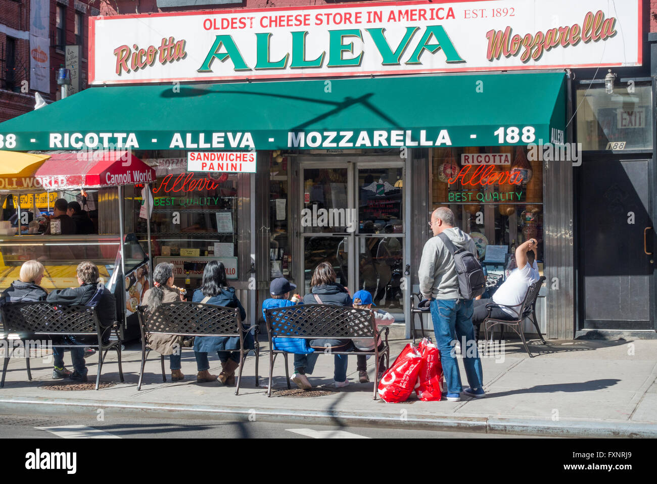 Tourists in Little Italy eating snacks on benches outside of Alleva Italian deli in New York City Stock Photo