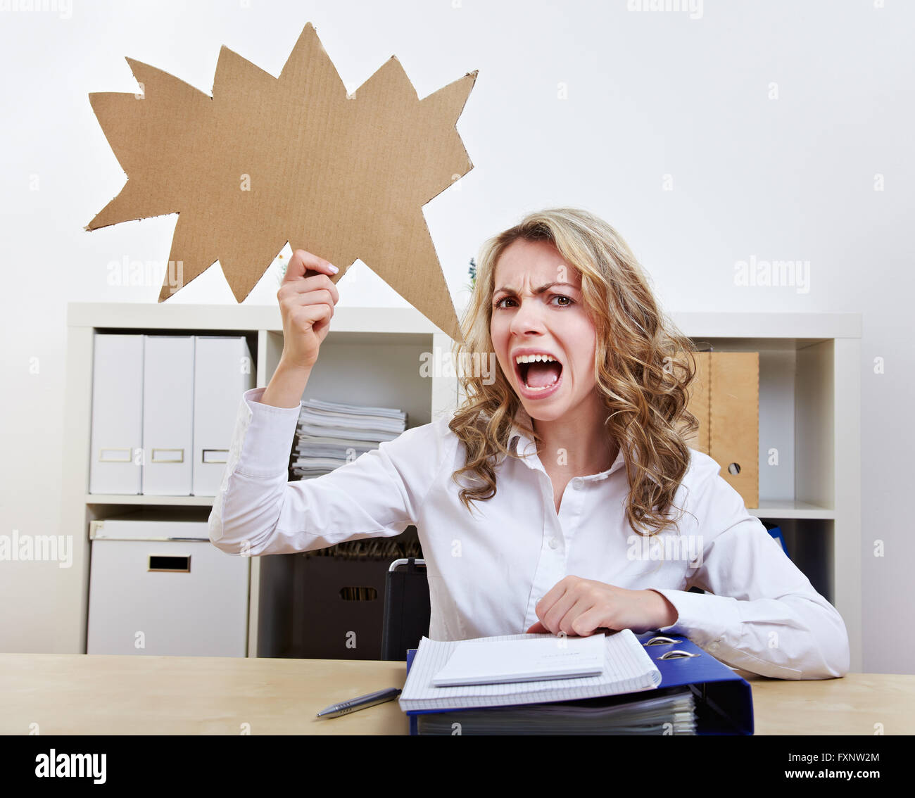 Angry woman sitting with empty jagged speech balloon in her office Stock Photo