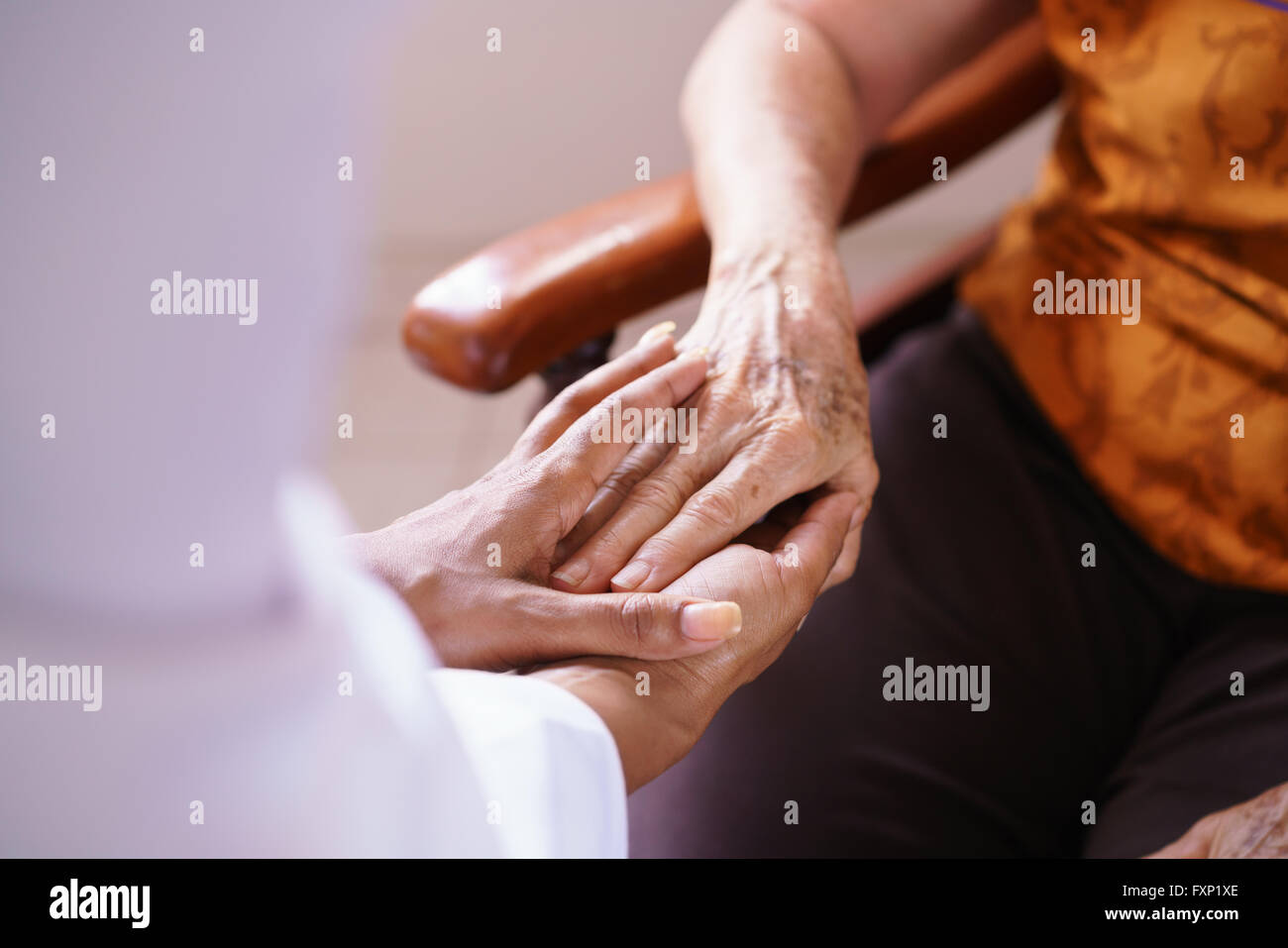 Old people in geriatric hospice: Black doctor visiting an aged patient, holding hands of a senior woman. Concept of comfort and Stock Photo