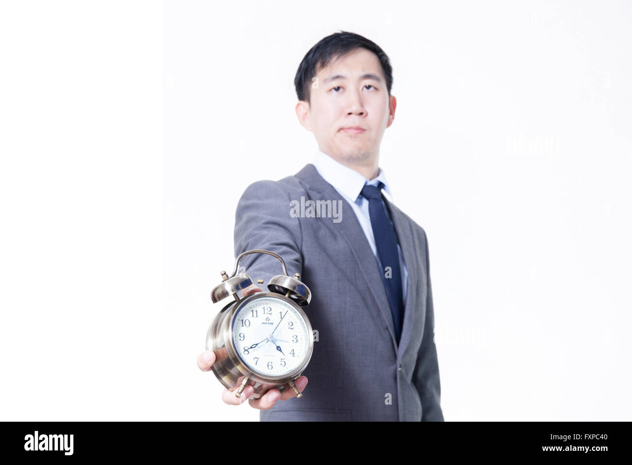 Young Asian businessman holding a clock in unpleasant face expression - business and time concept Stock Photo