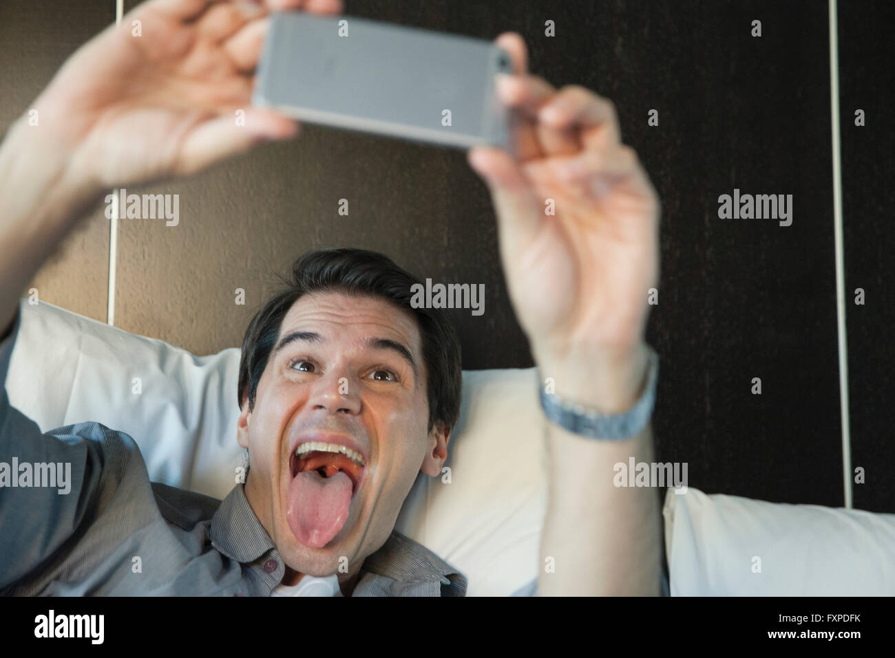 Man using smartphone to take a selfie, sticking out tongue Stock Photo