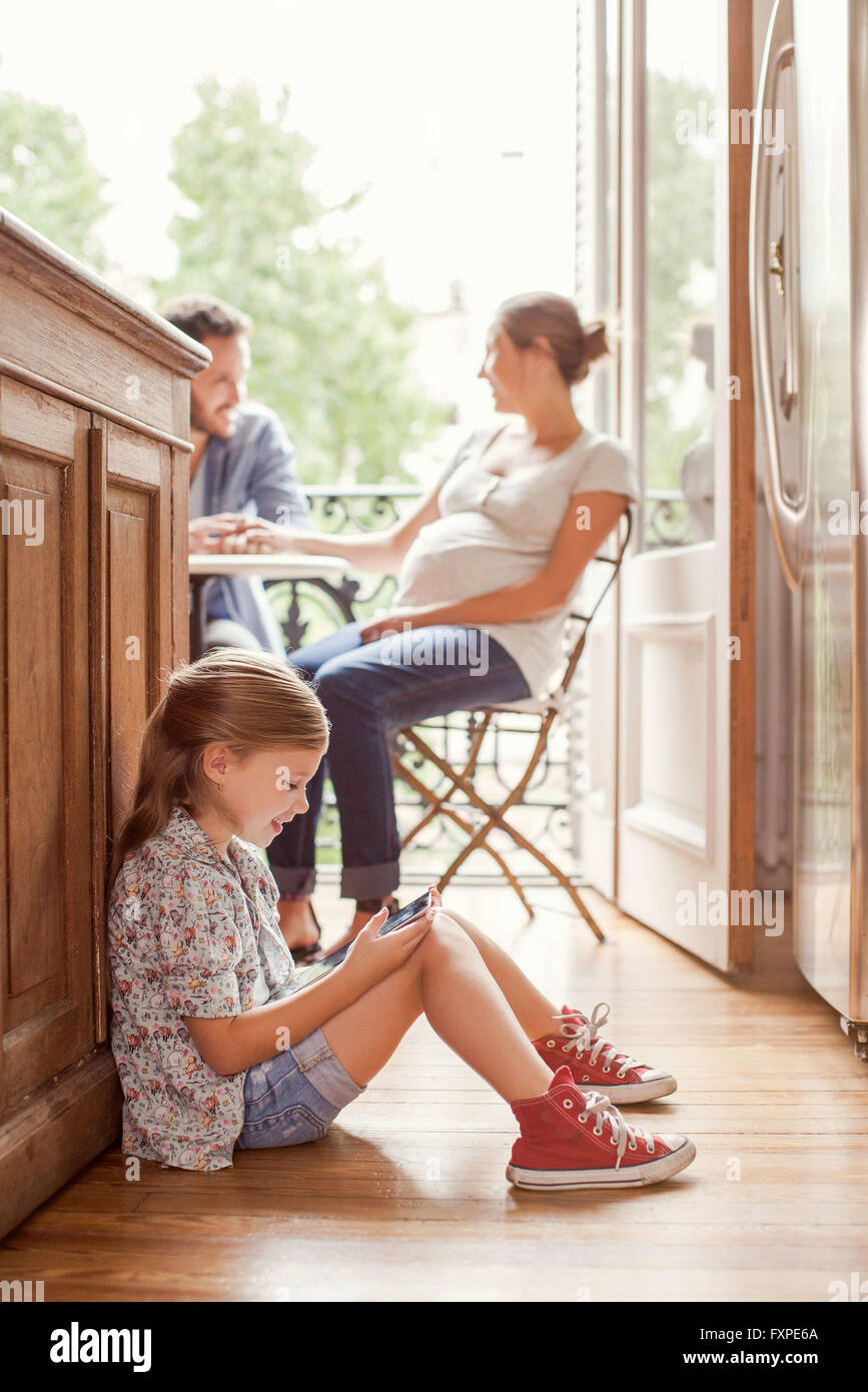 Girl engrossed in video game while parents chat in background Stock Photo