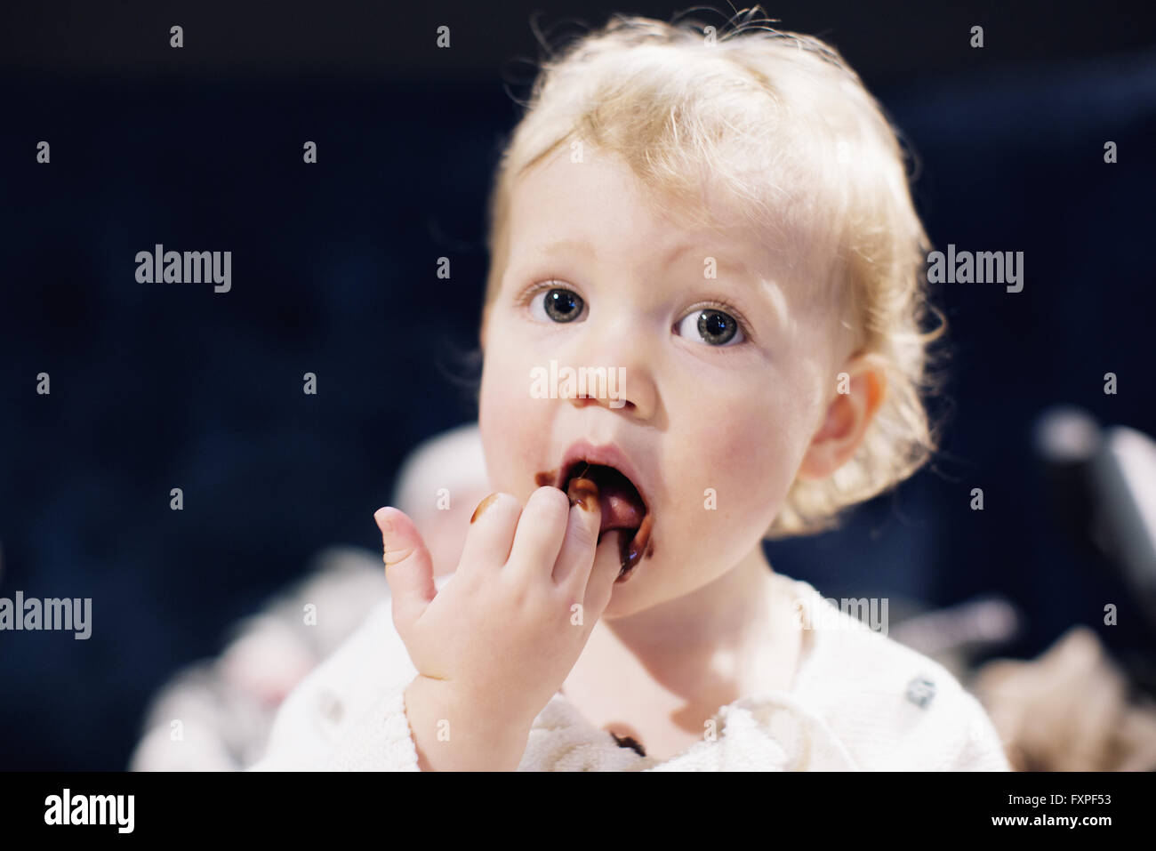 Toddler licking chocolate syrup from fingers Stock Photo