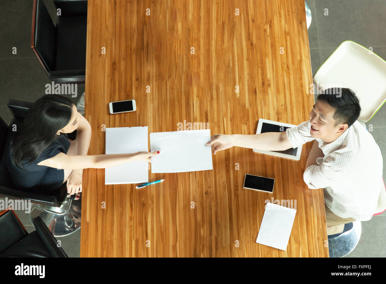 Top View of Business People sitting behind meeting desk, handing out documents Stock Photo