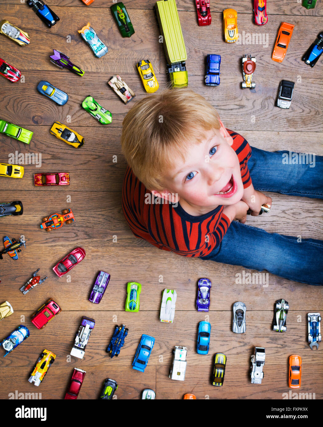 boy looking up at camera surrounded by toy cars Stock Photo